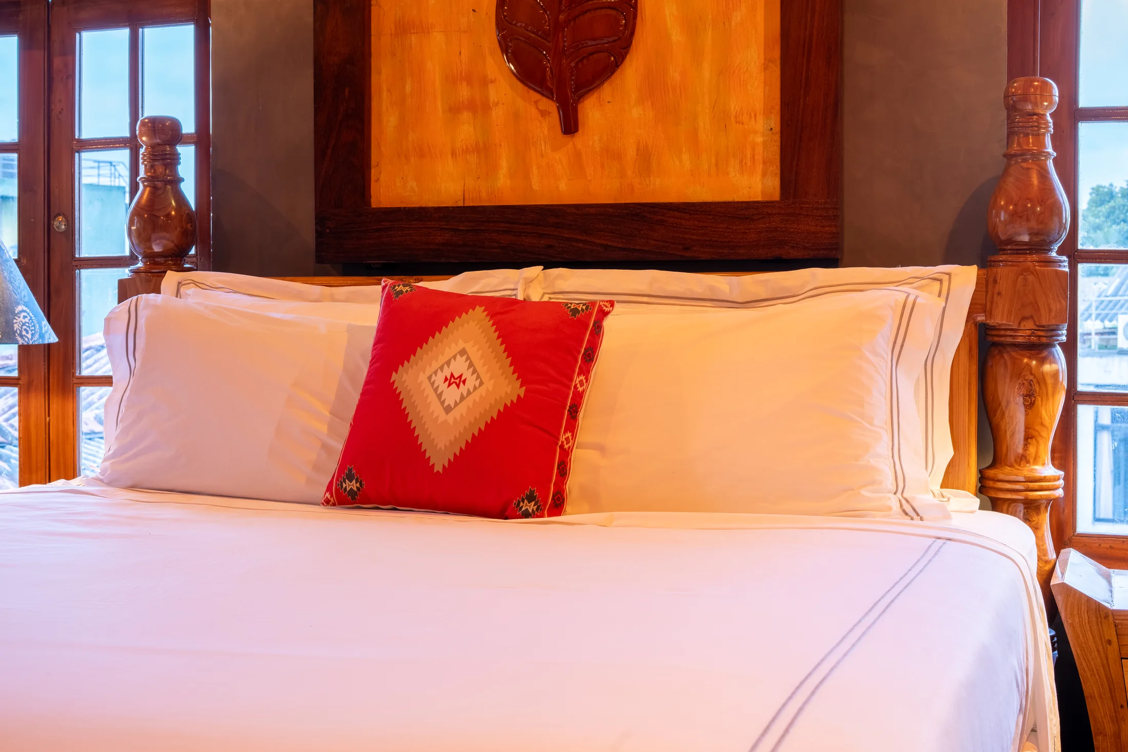 Close view of the bed's carved headboard and red Sri Lankan accent cushion